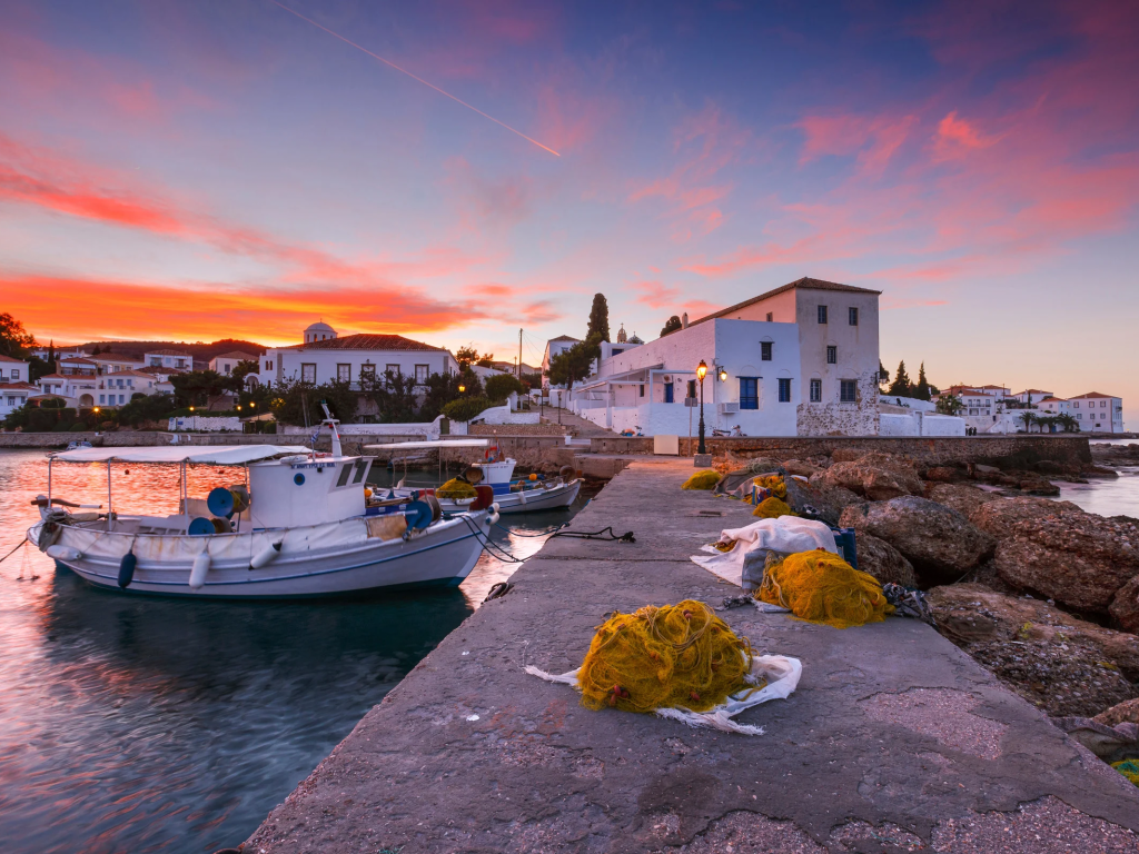 Bellissimo tramonto sul porto di Spetses con barche ormeggiate e reti da pesca sul molo.