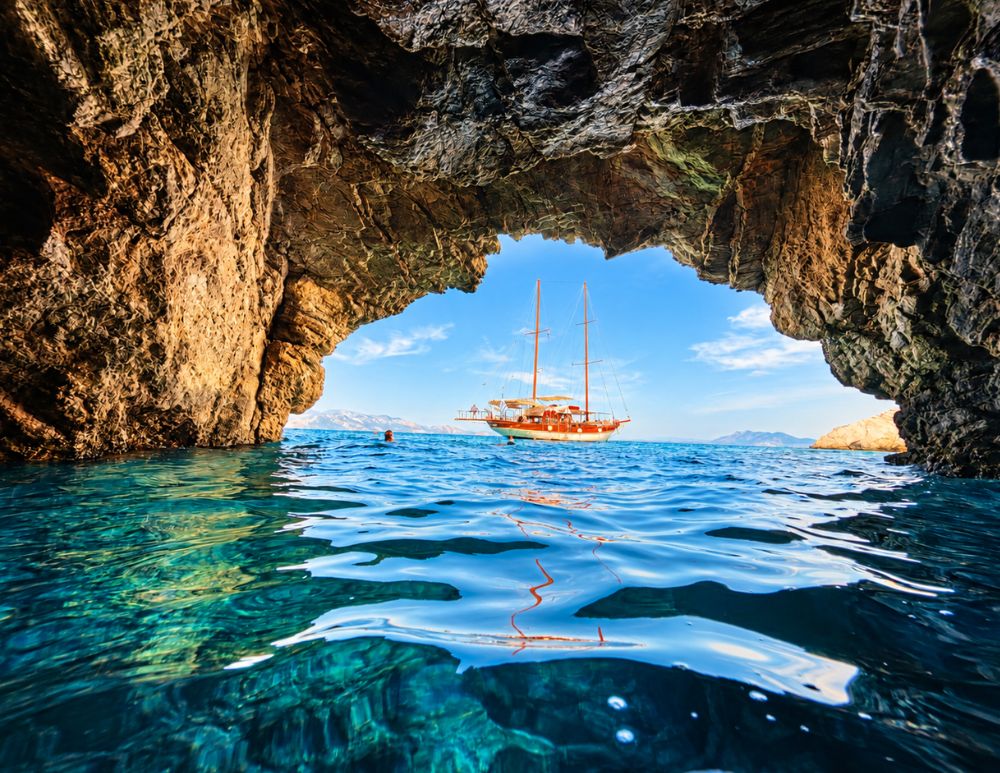 Vista dall'interno della Grotta delle Foche (Seal Cave) a Symi, con l'imbarcazione Poseidon al largo, incorniciata dalle pareti rocciose della grotta e dalle acque cristalline del Mar Egeo.