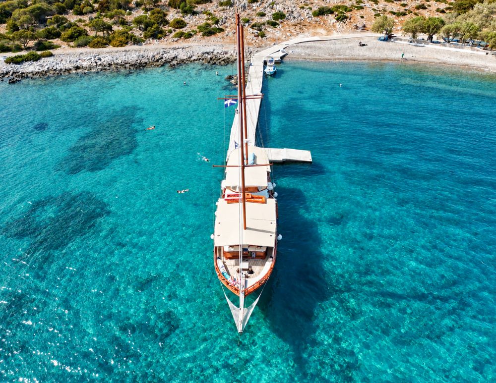 Imbarcazione Poseidon attraccata al molo dell'isoletta di Seskli, a Symi, circondata dalle acque turchesi e cristalline del Mar Egeo.